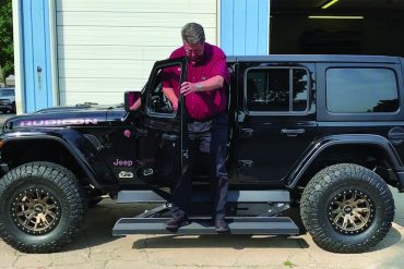 Driver testing electric running boards on a black Jeep Rubicon