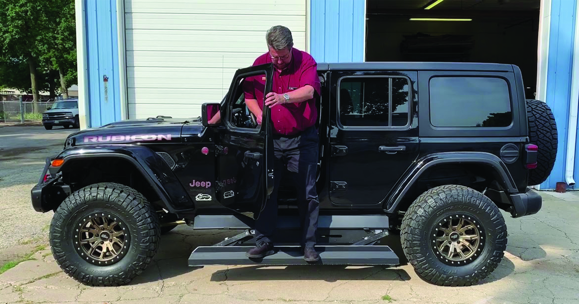 Driver testing electric running boards on a black Jeep Rubicon